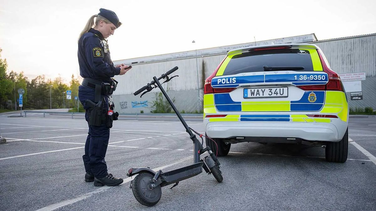 Policijos pareigūnas stovi šalia elektrinio paspirtuko Švedijos gatvėje.